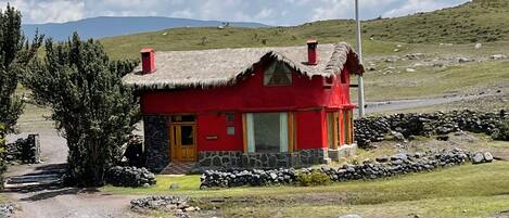 Una casa roja con techo de paja, paredes de piedra y valla de piedra en un entorno rural.