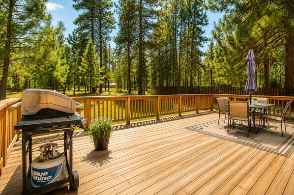 Une terrasse en bois avec un barbecue, des chaises et un parasol.