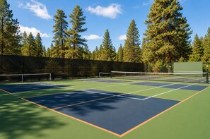 Ein Tennisplatz mit mehreren Spielfeldern, umgeben von Bäumen und einem Zaun.