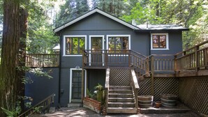 A two-story cabin with a wooden deck and a staircase leading to the upper floor. - Stairway to Haven ~ Family Cabin in Monte Rio (Monte Rio)