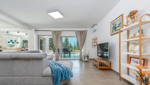 A modern living room with a grey sofa, a TV, and a wooden bookshelf. - Villa Molaris (Preko)