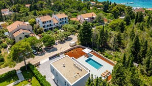 An aerial view of a coastal area with multiple buildings, a swimming pool, and a clear view of the sea. - Villa Molaris (Preko)