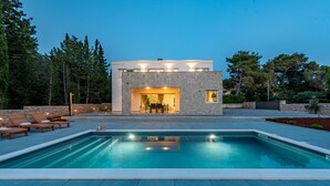 A modern house with a swimming pool, stone exterior, and a patio with lounge chairs. - Villa Molaris (Preko)