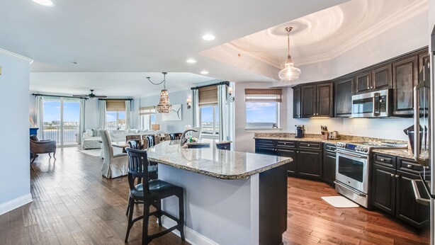A spacious kitchen with dark wood cabinets, stainless steel appliances, and a large island with bar stools. - The Pass 608 by Liquid Life (Orange Beach)