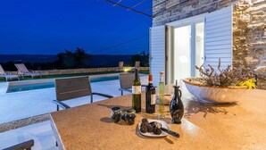 Un área de comedor al aire libre con piscina, muros de piedra y vistas al mar.
