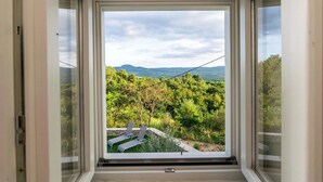 Una habitación con un amplio ventanal que ofrece vistas a un paisaje verde y exuberante y montañas a la distancia.