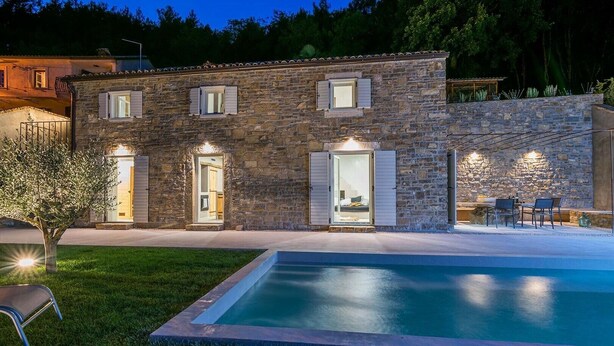 Un edificio de piedra con piscina, mobiliario de exterior e ingreso bien iluminado.