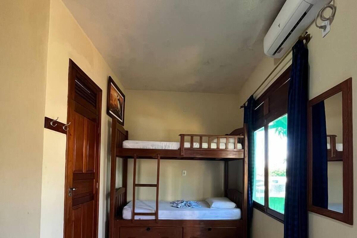 A room with bunk beds, a wooden door, a window with curtains, and an air conditioning unit.
