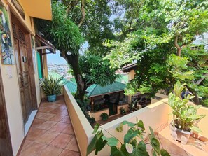 A balcony with potted plants, a view of the city, and a traditional building with a green roof. - Hostel Manaus (Manaus)