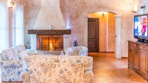 A living room with a fireplace, floral-patterned sofas, a television, and a wooden cabinet.