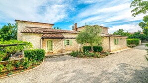 A stone house with a tiled roof, a gravel driveway, and a garden with various plants and flowers.