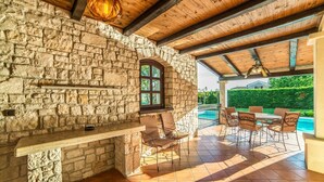 A stone-walled patio with a pool, outdoor seating, and a wooden ceiling.