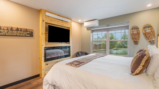 A bedroom with a large bed, a wooden wall unit with a TV, a window with a view, and a motivational quote on the wall.