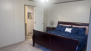 A bedroom with a wooden bed, a ceiling fan, a nightstand with a lamp, and a door leading to another room.