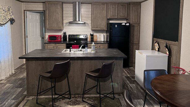 A compact kitchen with a central island, two bar stools, a refrigerator, a microwave, and a stove.