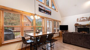 Amplia sala de estar con una mesa de comedor de madera, sillas, chimenea y ventanas grandes con persianas.