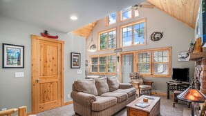 A cozy living room with a large wooden door, a brown sofa, a fireplace, and a television.