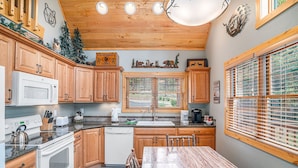 A kitchen with wooden cabinets, a white stove, a microwave, and a sink. There are decorative items on the wall and a window with blinds.