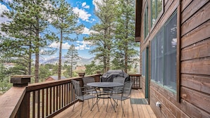 A wooden deck with a round table and chairs, overlooking a mountainous landscape.