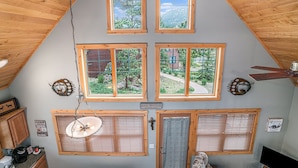 A cabin with four windows offering views of a mountainous landscape, a ceiling fan, and a sign indicating the cabin's location within Rocky Mountain National Park.