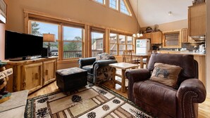 A spacious living area with a large window, a television, a leather sofa, and a dining table.