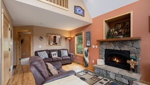 A living room with a stone fireplace, a brown leather sofa, and a wooden coffee table.