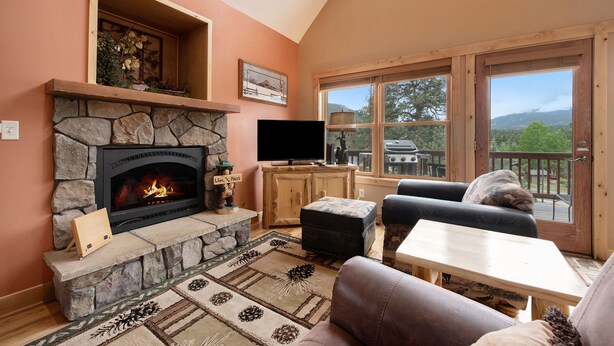 A cozy living room with a stone fireplace, comfortable seating, and a large window offering a scenic view.