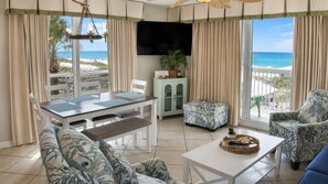 Ein Zimmer mit Esstisch, Stühlen, einer Couch, einem Fernseher und Blick auf den Strand.