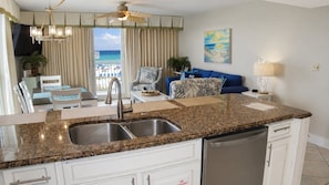 A kitchen with a granite countertop, stainless steel sink, and white cabinetry.