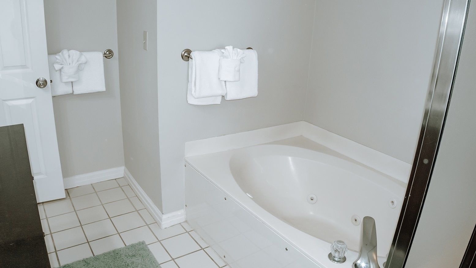 Un baño con una bañera blanca, dos toallas en percheros y un felpudo verde en el suelo.