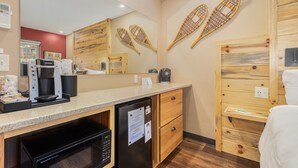 Hotellihuone, jossa on pieni keittiönurkkaus, puuhuonekalut ja suuri peili, joka heijastaa huonetta.