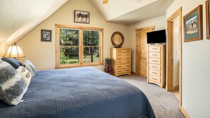 A bedroom with a large bed, a ceiling fan, a dresser, a television, and a window with a view of the outdoors. - Solitude Bobcat #6 - Estes Park 2 Bedroom Condo by RedAwning (Estes Park)