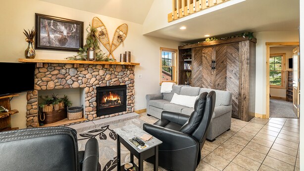 A living room with a stone fireplace, a gray sofa, a leather chair, and a television. - Solitude Bobcat #6 - Estes Park 2 Bedroom Condo by RedAwning (Estes Park)