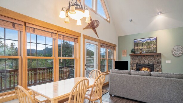 A spacious living area with a fireplace, a dining table with chairs, and large windows offering a view of the outdoors. - Solitude Eagle #2 - Estes Park 2 Bedroom Condo by RedAwning (Estes Park)