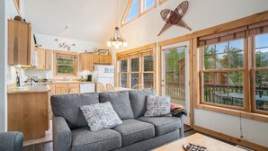 A cozy living room with a grey sofa, wooden dining table, and large windows offering a view of the outdoors. - Solitude Eagle #2 - Estes Park 2 Bedroom Condo by RedAwning (Estes Park)
