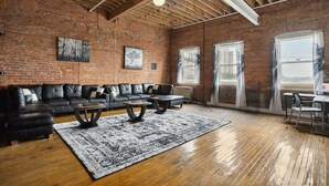 A spacious living room with a brick wall, a black leather sofa, a coffee table, and a large rug. - Downtown Detroit Loft - Fully equipped & Absolutely Gorgeous theme by RedAwning (Detroit)