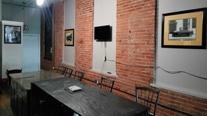 A conference room with a brick wall, a flat-screen TV mounted on the wall, and framed pictures on the wall. - Downtown Detroit Loft - Fully equipped & Absolutely Gorgeous theme by RedAwning (Detroit)
