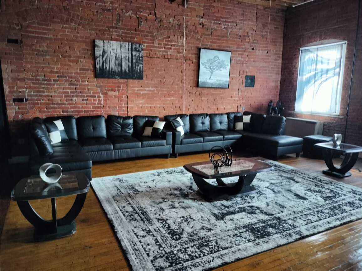 A living room with a brick wall, a black leather sofa, a coffee table, and a patterned rug.