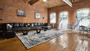 A spacious living room with a brick wall, a sectional sofa, a coffee table, and a large rug. - Downtown Detroit Loft - Fully equipped & Absolutely Gorgeous theme by RedAwning (Detroit)