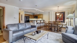 A modern living room with a grey sofa, a wooden coffee table, and a dining area with wooden chairs and a bar. - 1BR Plus Den, Heart of Beaver Creek Village 1 Bedroom Condo by RedAwning (Avon)