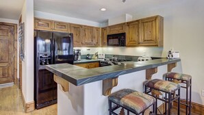 A kitchen with wooden cabinets, a stainless steel refrigerator, a microwave, a stove, and a bar stool. - 1BR Plus Den, Heart of Beaver Creek Village 1 Bedroom Condo by RedAwning (Avon)