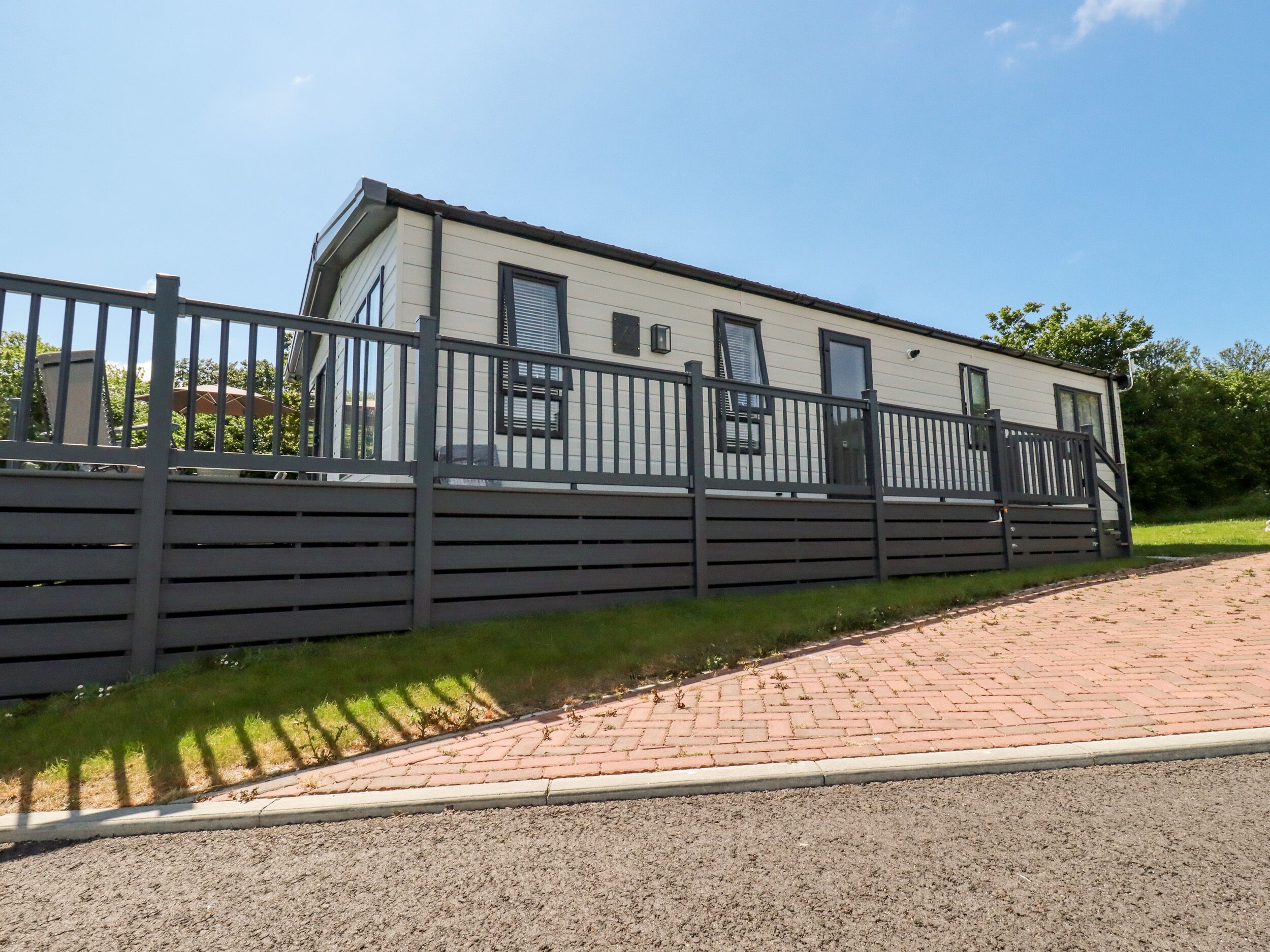 A single-story mobile home with a dark fence, a paved driveway, and a grassy area.