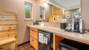 A modern kitchen with wooden cabinetry, a built-in dishwasher, a coffee maker, and a mirror above the counter. - Solitude Bear Room Ada 103 - Estes Park 1 Bedroom Studio by RedAwning (Estes Park)