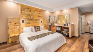 A hotel room with a large bed, wooden headboard, a desk with a mirror, and a small kitchenette. - Solitude Bear Room Ada 103 - Estes Park 1 Bedroom Studio by RedAwning (Estes Park)