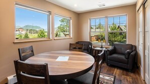 A room with a round wooden table, two leather sofas, and large windows offering a view of greenery and buildings.
