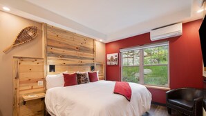 Ein Schlafzimmer mit einem großen Bett, einem Holzkopfteil, einem Fenster mit Blick und einem schwarzen Ledersessel sowie einer Klimaanlage.