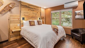 A bedroom with a wooden headboard, a large bed with white bedding, a nightstand, a chair, and a window with a view of greenery. - Solitude Gem Lake 203 - Estes Park 1 Bedroom Studio by RedAwning (Estes Park)