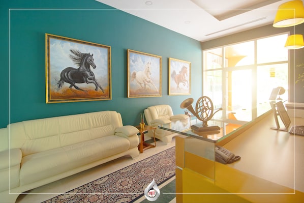 A living room with a teal wall, a white sofa, a glass coffee table, and three framed horse paintings.