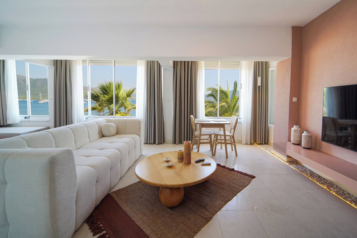 A modern living room with a sofa, a round wooden table, and a TV on the wall.