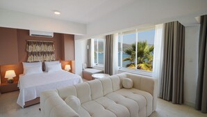 A hotel room with a bed, a sofa, a small table, and a view of the sea.